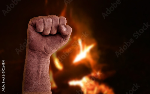 Raised clenched fist with burning flames from bonfire in background. Stock photo with socialism, communism, revolution, workman and power to the people concept  photo