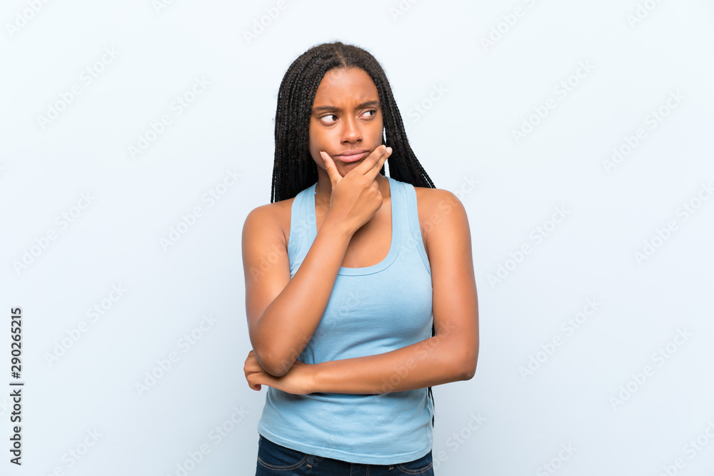 African American teenager girl with long braided hair over isolated blue background thinking an idea African American teenager girl with long braided hair over isolated blue background thinking an idea