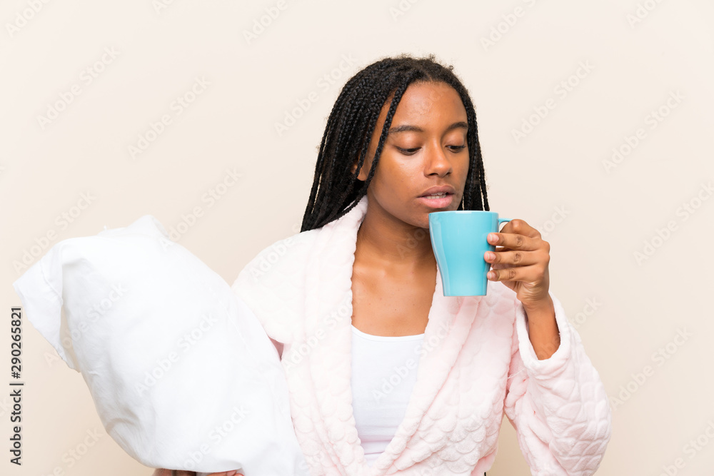 African American teenager girl with long braided hair in pajamas over isolated background and holding a cup of coffee African American teenager girl with long braided hair in pajamas over isolated background and holding a cup of coffee