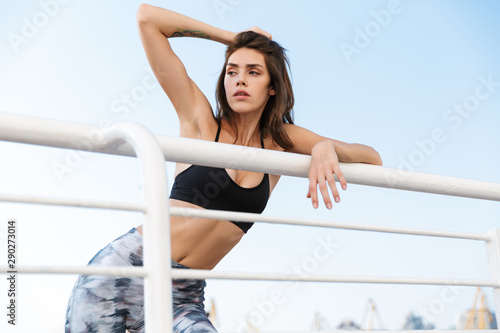 Image of young sexual woman looking aside while bending on railing outdoors