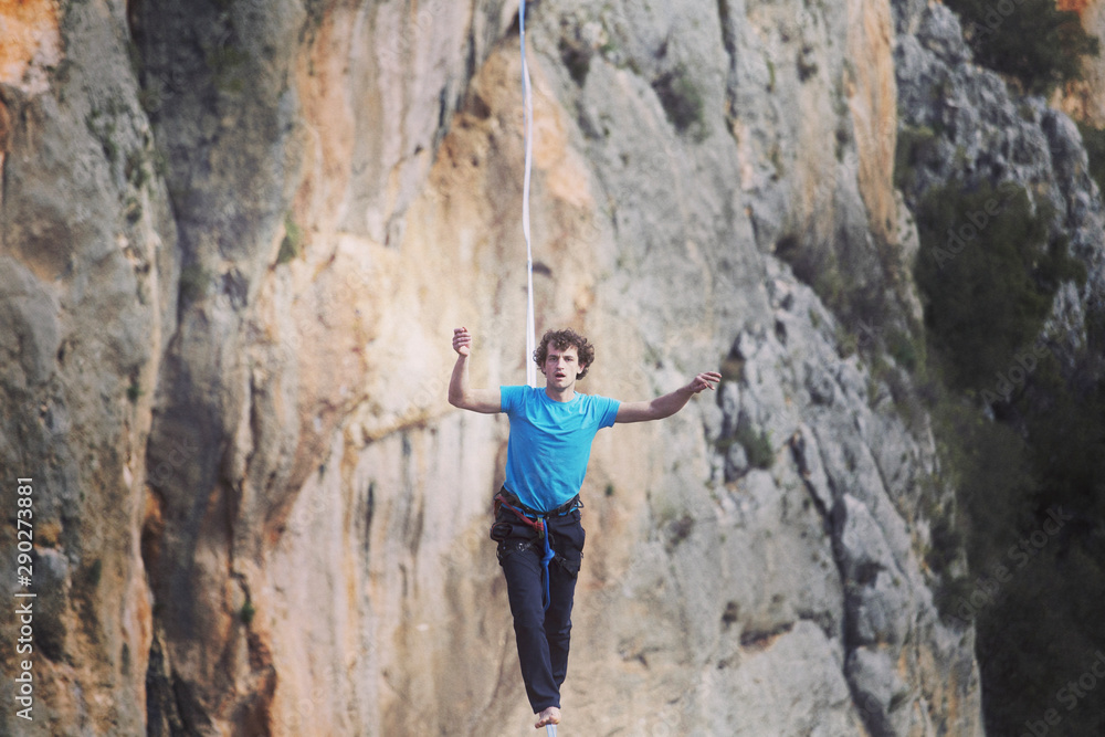 A man is walking along a stretched sling. Highline in the mountains. Man catches balance. Performance of a tightrope walker in nature. Highliner on the background of the mountains.