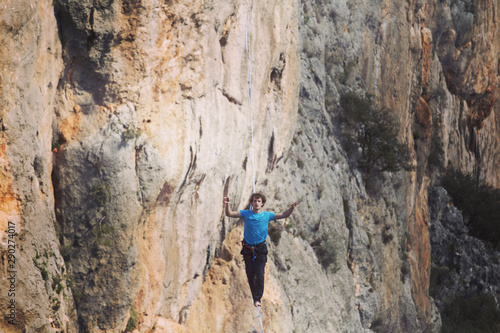 A man is walking along a stretched sling. Highline in the mountains. Man catches balance. Performance of a tightrope walker in nature. Highliner on the background of the mountains.