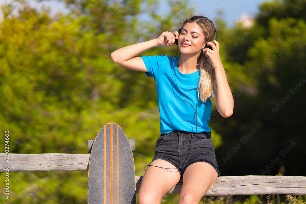 Young teenager girl with skate listening to music with headphones at outdoors