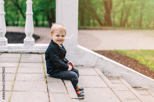 Portrait handsome boy with with smiling face sitting on stone steps at the park in summer. Child relaxing outdoors in spring or summer