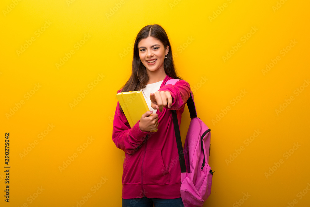 Fototapeta premium Teenager student girl on vibrant yellow background points finger at you