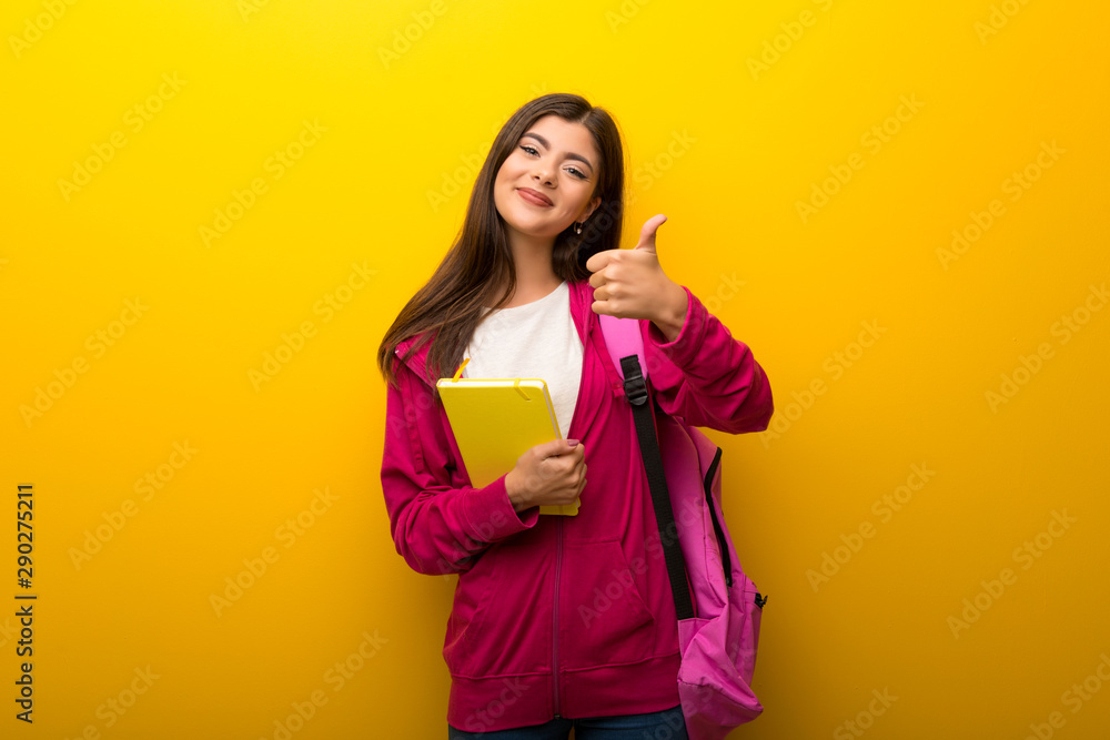 Teenager student girl on vibrant yellow background giving a thumbs up gesture and smiling Teenager student girl on vibrant yellow background giving a thumbs up gesture and smiling