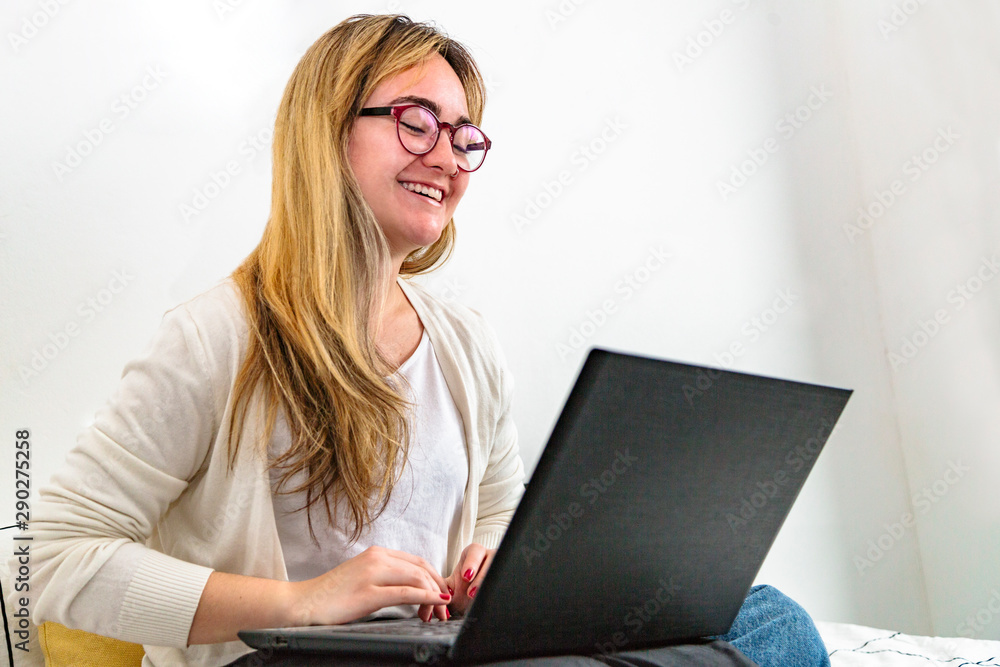 Young smiling woman working on laptop in bedroom Young smiling woman working on laptop in bedroom