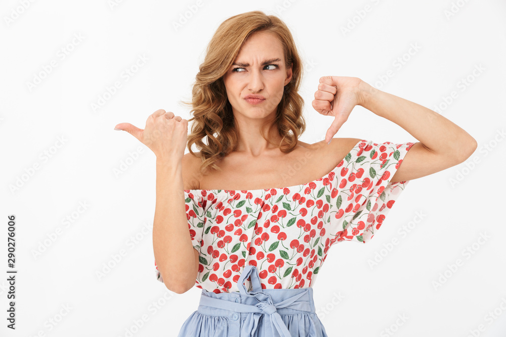 Portrait of young displeased woman wearing summer clothes grimacing and gesturing thumb down and aside over white background in studio Portrait of young displeased woman wearing summer clothes grimacing and gesturing thumb down and aside over white background in studio