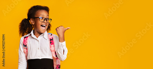 Excited Black Schoolgirl Pointing Thumbs At Copy Space In Studio