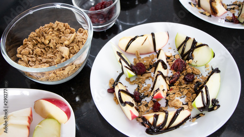 Healthy snack homemade: red and green apple, oat granola, whole grain and berries with chocolate syrup on top in a white bowl. Balanced diet and healthy eating concept. photo