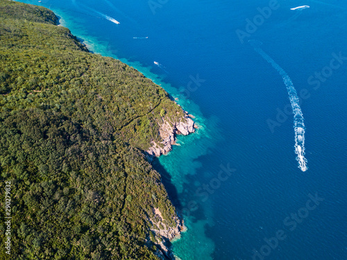 Aerial view of boats and watercraft off the coast of jagged and lush Mediterranean vegetation. Sea, crystal clear water. Sveti Nikola, Budva island, Montenegro