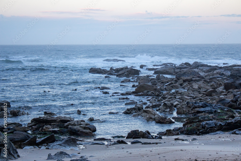 Atlantic Ocean coast in Portugal in the morning. Seascape in blue morning fog. Ocean beach with stones and waves. Empty beach. Rocky coastline. Calm ocean shore. Wild nature concept. 