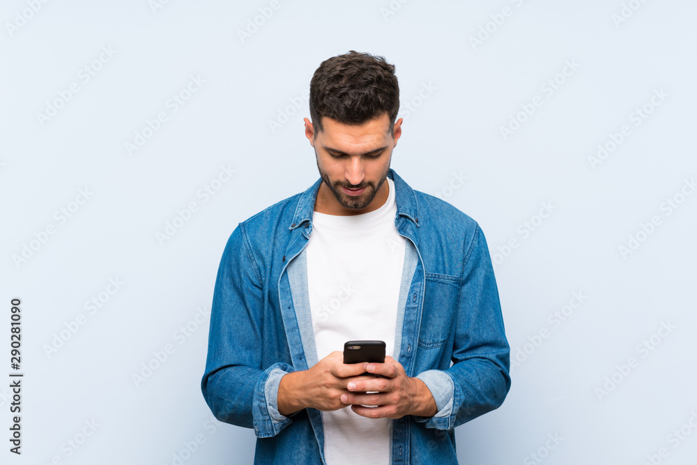 Handsome man over isolated blue background sending a message with the mobile Handsome man over isolated blue background sending a message with the mobile