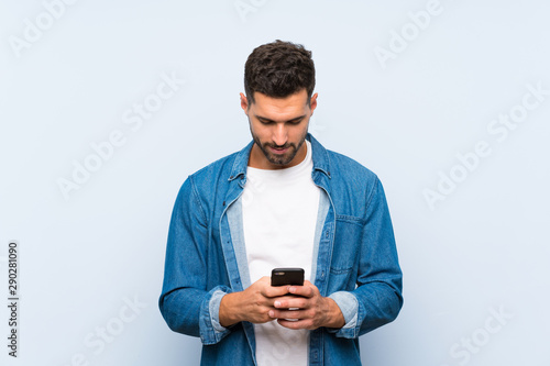 Handsome man over isolated blue background sending a message with the mobile