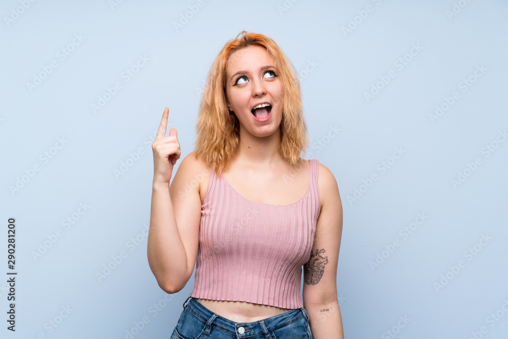 Young woman over isolated blue background pointing up and surprised Young woman over isolated blue background pointing up and surprised