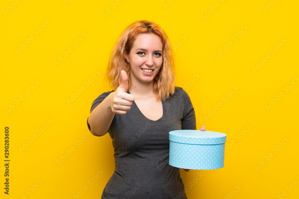 Young woman over isolated yellow background holding gift box Young woman over isolated yellow background holding gift box