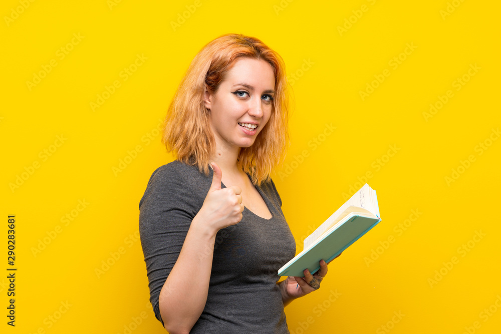 Young woman over isolated yellow background holding and reading a book Young woman over isolated yellow background holding and reading a book