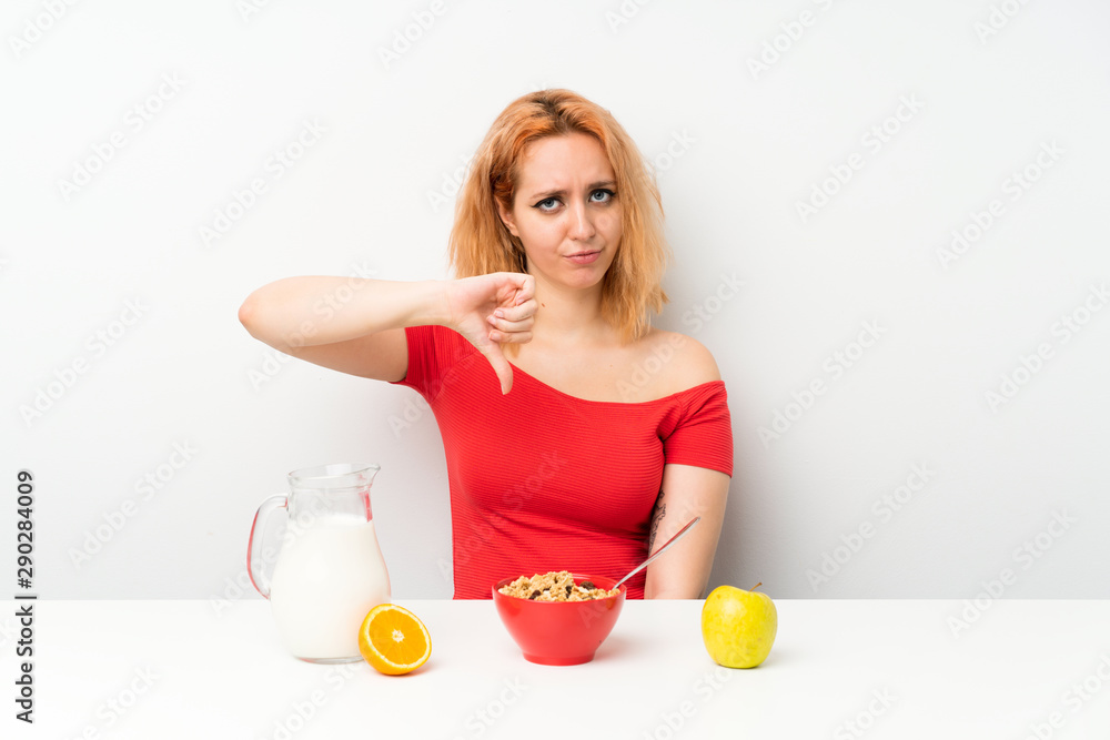 Young woman having breakfast showing thumb down sign Young woman having breakfast showing thumb down sign