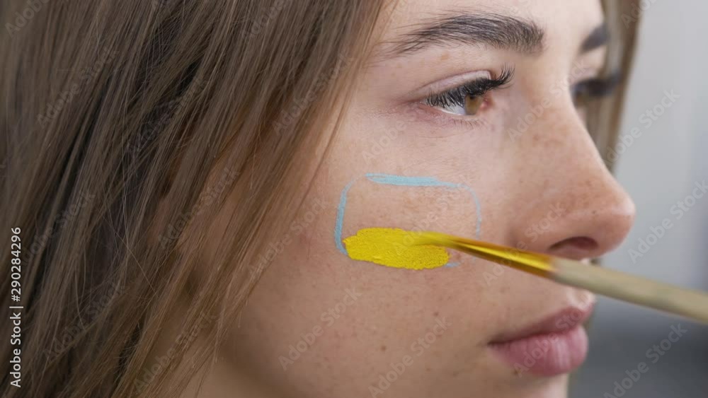 Detailed portrait of a young beautiful woman. Artist painting on the girl's face using small soft brush. Body art concept. Cute artwork on a humans body Detailed portrait of a young beautiful woman. Artist painting on the girl's face using small soft brush. Body art concept. Cute artwork on a humans body