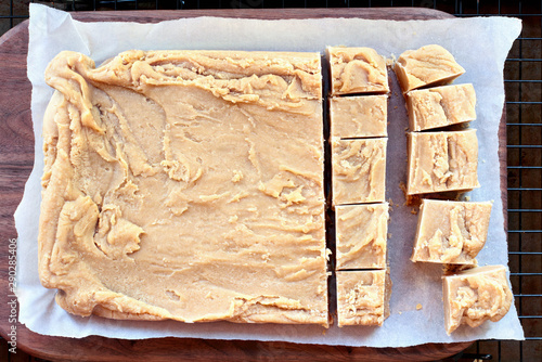 Whole block of delicious, homemade peanut butter fudge over a rustic wood cutting board being cut into squares.