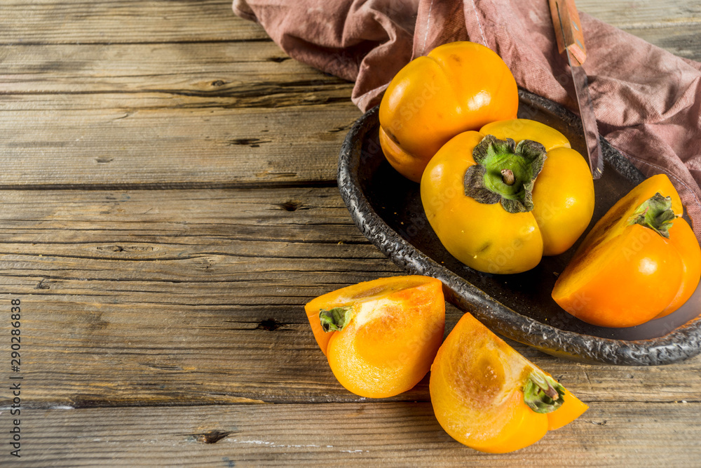 Whole and sliced persimmons, fresh organic farm fruit on rustic wooden background. Isolated, copy space