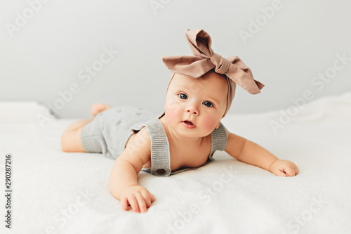 Beautiful baby lies on bed smiling bow on her head.