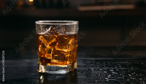 Fototapeta Naklejka Na Ścianę i Meble -  Glass of Whisky (whiskey), bourbon, ice tea or coke (cola) soda with ice and water drops on wood table at dark background with copy space