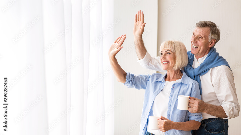 Obraz premium Happy senior couple looking through window and hugging