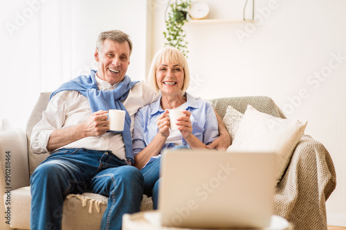 Mature couple watching film on laptop and drinking coffee