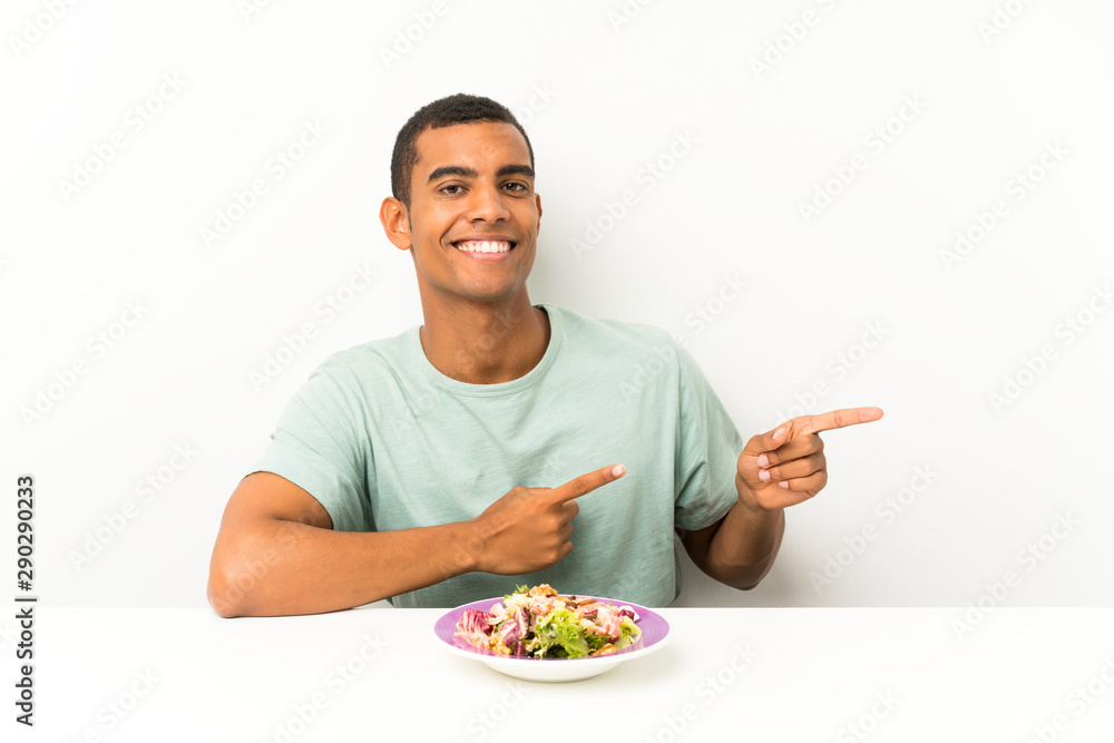 Young handsome man with salad in a table pointing finger to the side Young handsome man with salad in a table pointing finger to the side
