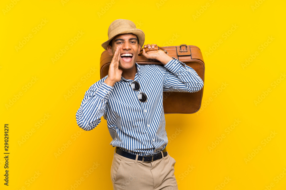 Brunette man holding a vintage briefcase over isolated yellow background shouting with mouth wide open