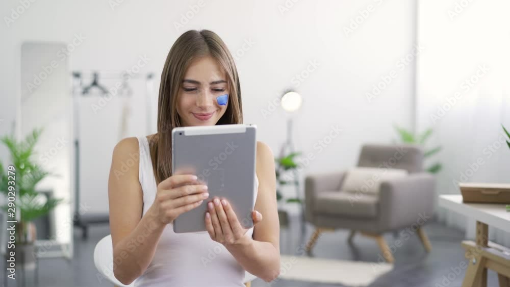 Portrait of young attractive woman with blue painted social media icon on her face looking in her tablet and smiling. Addiction to gadgets. Portrait of young attractive woman with blue painted social media icon on her face looking in her tablet and smiling. Addiction to gadgets.