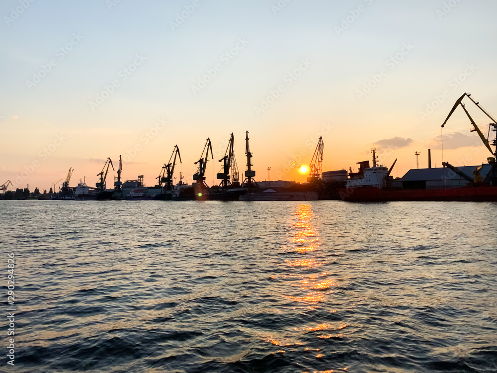 River port with ships at sunset. Busy traffic artery. Logistics and infrastructure. Loading and unloading of ships, trade traffic. Industry and economics. Plants and factories. Transport hub. Dnipro