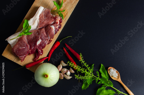 Fototapeta Naklejka Na Ścianę i Meble -  Raw pork on a wooden plate and spices placed on a black background, preparing ingredients before cooking, Thai food,Stir-fried pork with basil leaves