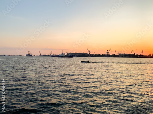 River port with ships at sunset. Busy traffic artery. Logistics and infrastructure. Loading and unloading of ships, trade traffic. Industry and economics. Plants and factories. Transport hub. Dnipro © Andrii Yalanskyi