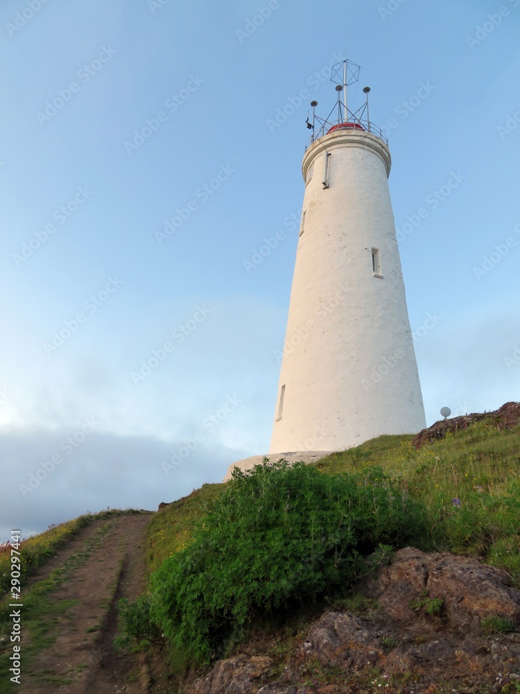 A lighthouse illuminated by the setting sun on a clear summer night in Reykjanes, Iceland