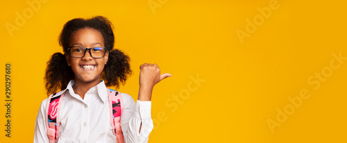 Afro School Girl Pointing Thumbs At Copy Space, Yellow Background photo