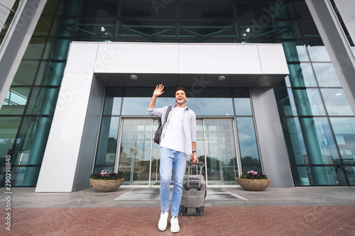 Happy man arrived home, waving hand while going out of airport building © Prostock-studio