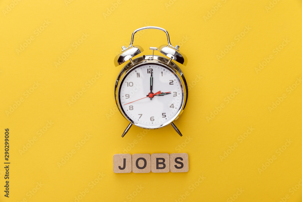 Φωτογραφία top view of clock and cardboard squares with jobs inscription on yellow backgrou