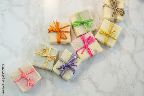 handmade organic soap in gift wax wrapping  paper with multi colored eco raffia ribbons on marble surface with space for text. Instagram style soap flat lay frame
