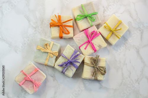 handmade organic soap in gift wax wrapping  paper with multi colored eco raffia ribbons on marble surface with space for text. Instagram style soap flat lay frame