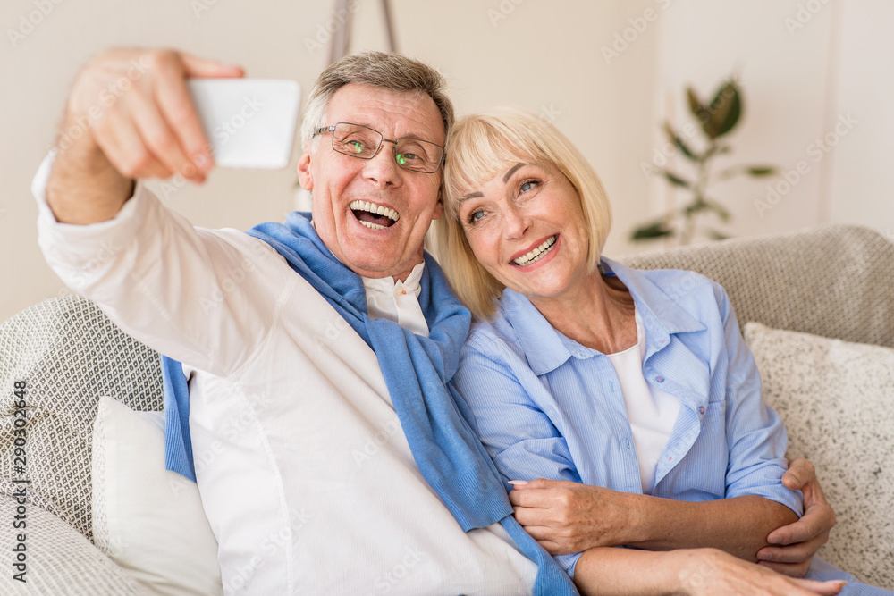 Modern grandparents taking selfie on cellphone, resting on sofa Modern grandparents taking selfie on cellphone, resting on sofa