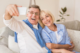 Modern grandparents taking selfie on cellphone, resting on sofa