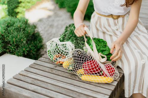 Girl holding mesh shopping bag and cotton shopper with vegetables without plastic bags, wooden background. Zero waste, plastic free concept. Sustainable lifestyle. Banner.