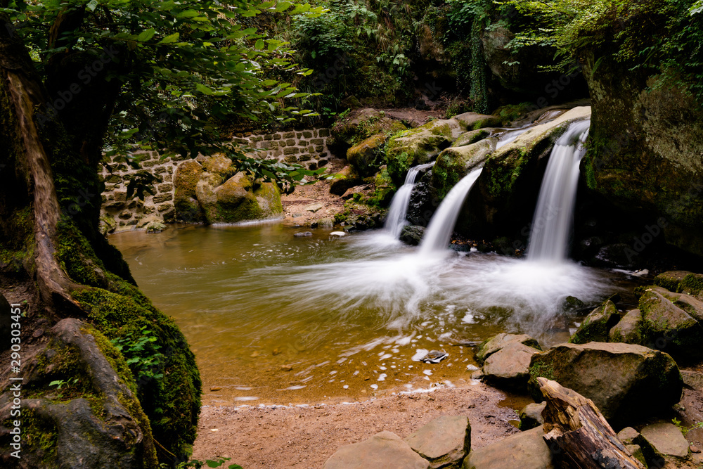 Fototapeta premium idyllic small waterfall in lush green forest landscape