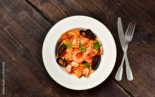 Spaghetti seafood pasta with clams and prawns with mussels and tomatoes in a white plate with on a wooden table. Recipe of Italian cuisine