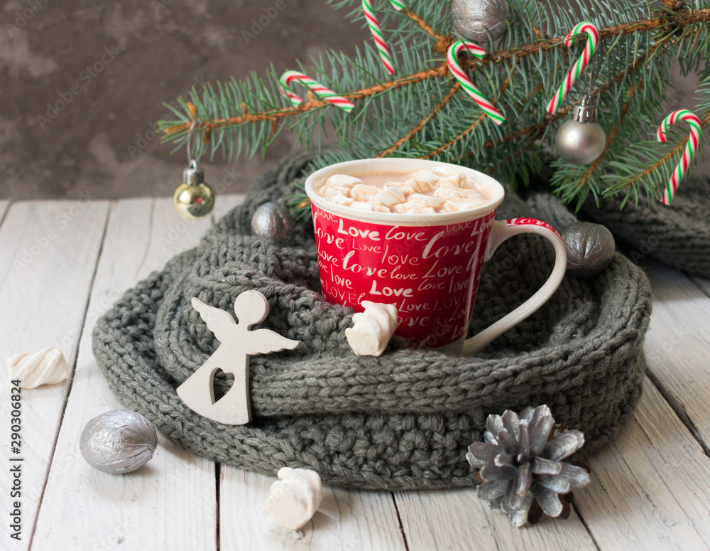Cup of hot cocoa or chocolate with marshmallows on the background of a knitted scarf and a branch of a Christmas tree. A traditional drink for the Christmas holidays. Cup of hot cocoa or chocolate with marshmallows on the background of a knitted scarf and a branch of a Christmas tree. A traditional drink for the Christmas holidays.