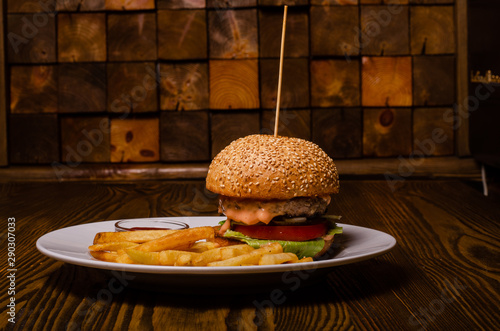 Tasty burger and french fries on plate, on wooden table background. Unhealthy food concept