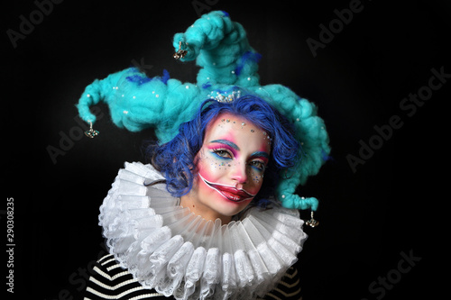 girl in makeup and costume jester . clown girl with bright makeup in blue wig On black background