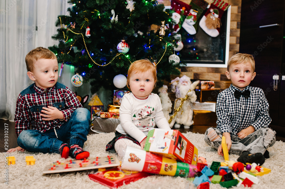 Happy family: children, kids, daughter and son, boy and girl unpack gifts near the Christmas tree and fireplace. New year concept. Merry Christmas. Happy family: children, kids, daughter and son, boy and girl unpack gifts near the Christmas tree and fireplace. New year concept. Merry Christmas.